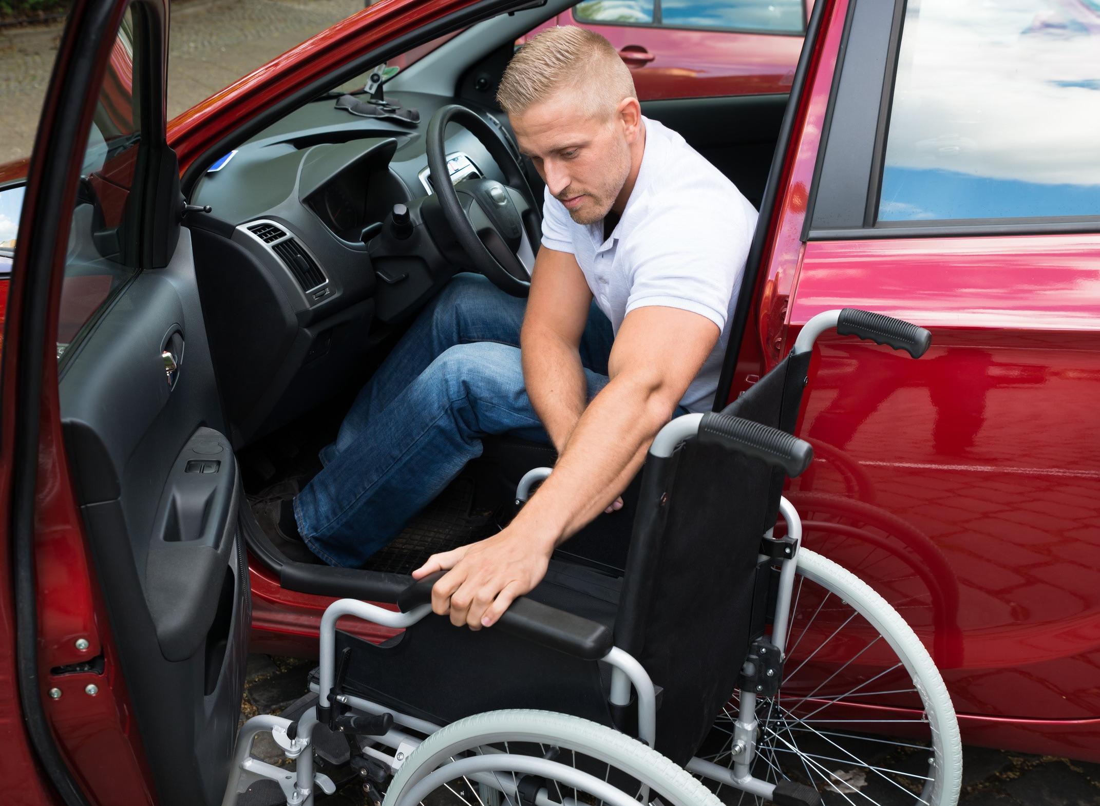 Ein Rollstuhlfahrer steigt ins Auto ein.