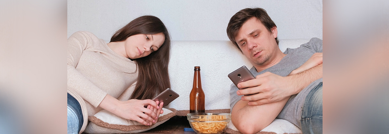Zwei jüngere Personen liegen auf dem Sofa und schauen auf ihre Smartphones.